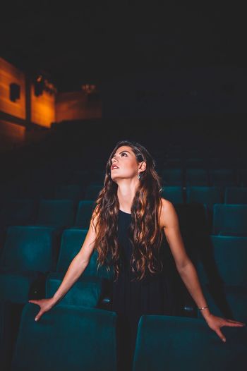 Beautiful young woman looking away while standing in movie theater
