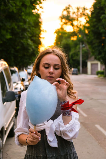 Cute and pretty young girl or student, eats and poses with sugar blue candy cotton on town street