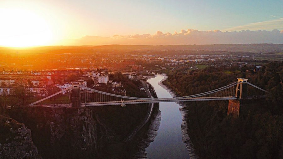 Sun rising in the distance behind clifton suspension bridge, bristol. captured via drone.