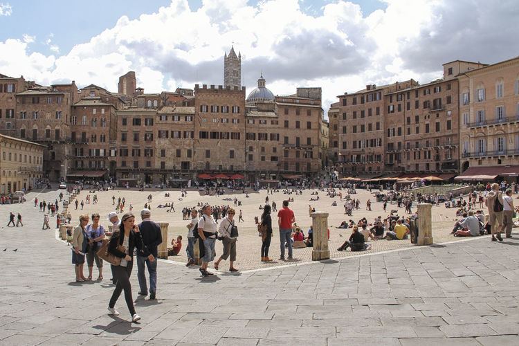 Tourist walking at piazza del campo against cloudy sky