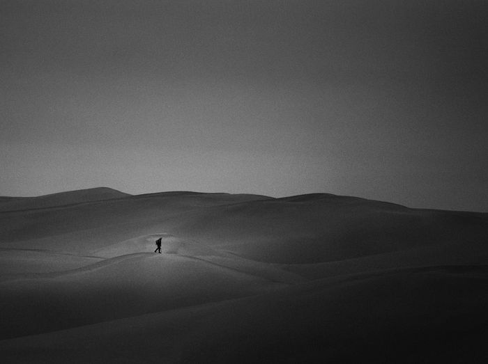 Man walking in desert against sky at dusk