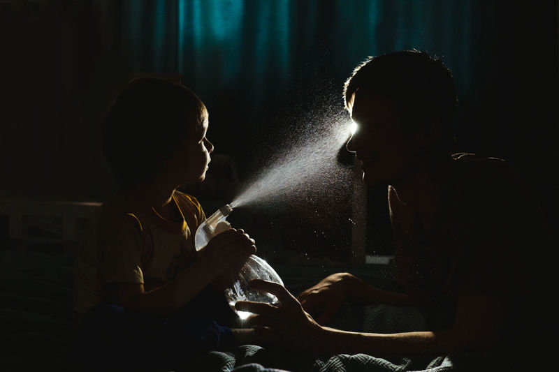Son spraying water on father in darkroom