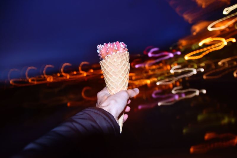 Cropped hand of man holding ice cream cone at night