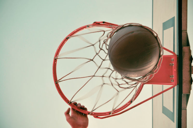 Cropped hand playing basketball against clear sky