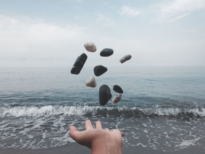 Cropped hand throwing pebbles in sea