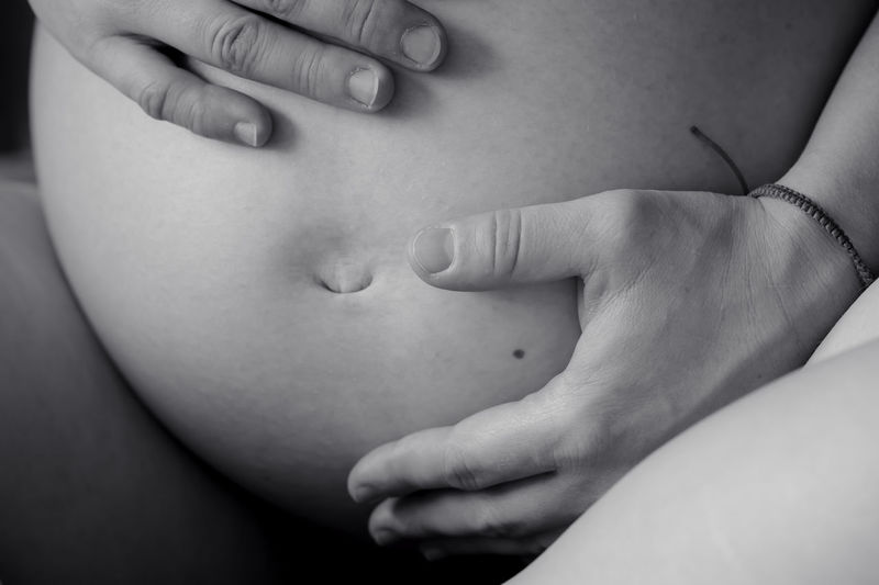 Midsection of naked pregnant woman with hands on stomach