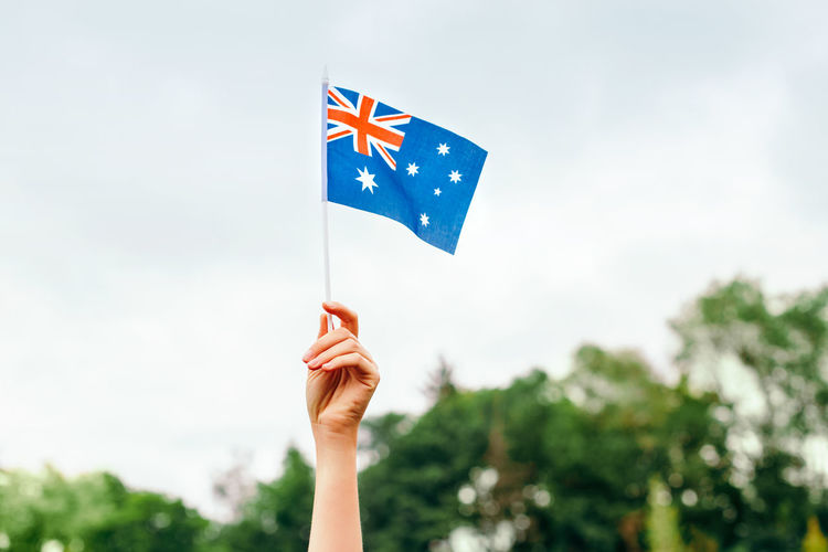 Close-up of hand holding  australian flag against blue sky. australia day celebration in january 