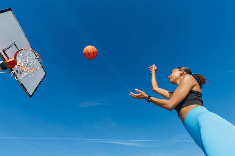 Sportswoman throwing basketball in hoop on sunny day