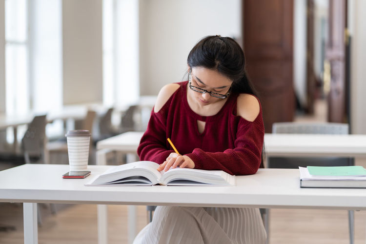 Smart asian girl writing outline while preparing for exam in reading room or classroom