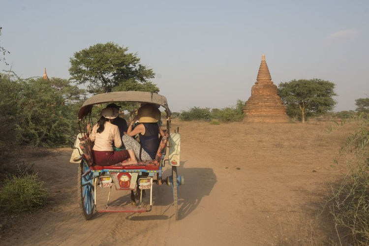 People traveling from cart on dirt road against temple