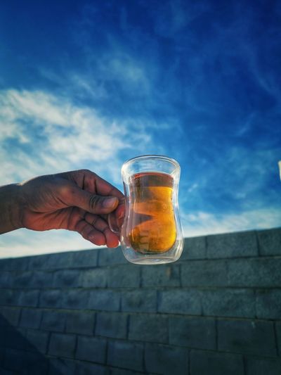 Midsection of person holding drink against sky