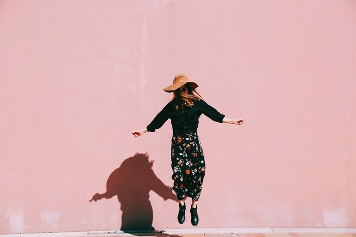 Woman jumping against pink wall
