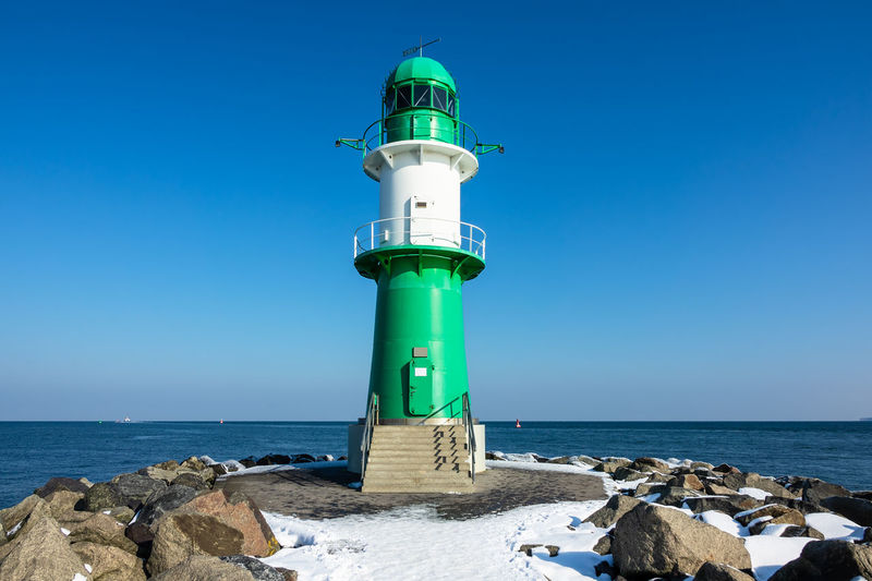 Lighthouse by sea against blue sky