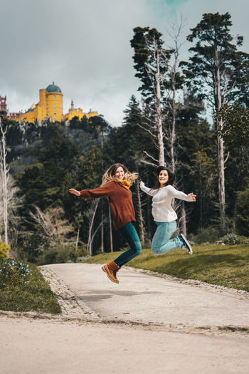 Portrait of beautiful females jumping on street against trees