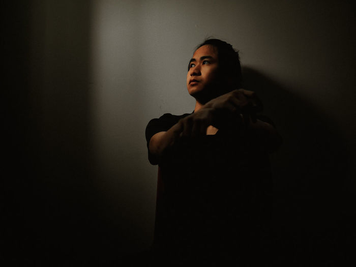 Young man looking away while standing against black background