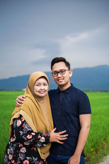 Portrait of young couple standing on field against sky