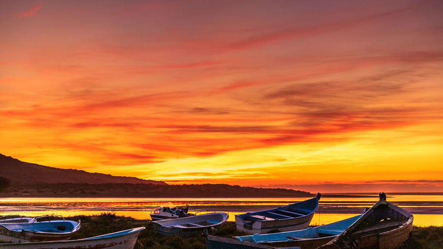 Boats moored in sea against orange sky