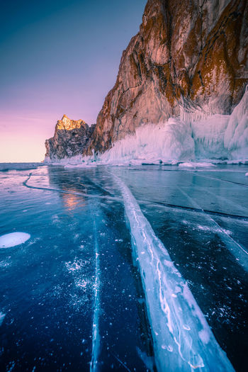 Scenic view of frozen lake by rock formation during sunset