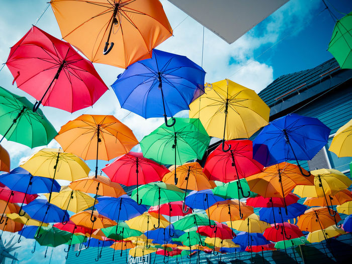 Low angle view of multi colored umbrellas hanging by building against sky