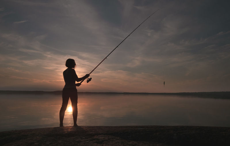 Silhouette of a fisherwoman with a fishing rod in her hands. active lifestyle theme