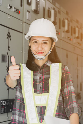 Portrait of woman gesturing while standing by electrical fuse