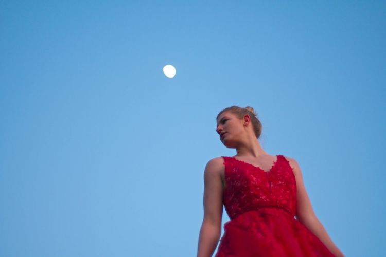 Low angle view of woman in red dress standing against clear blue sky