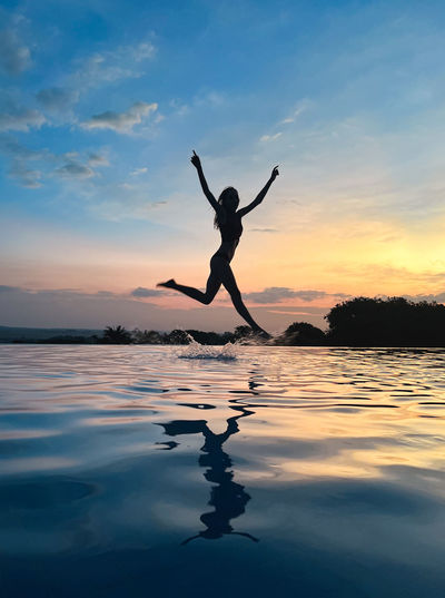 Side view of man jumping in lake during sunset