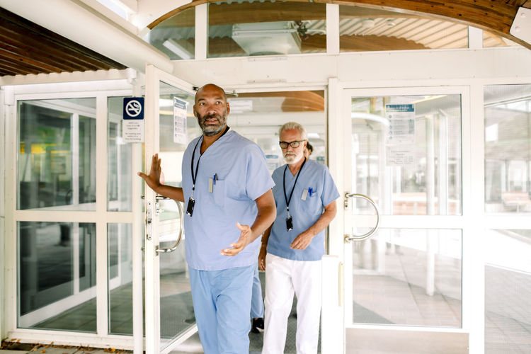 Mature nurse talking to senior colleague while holding hospital door