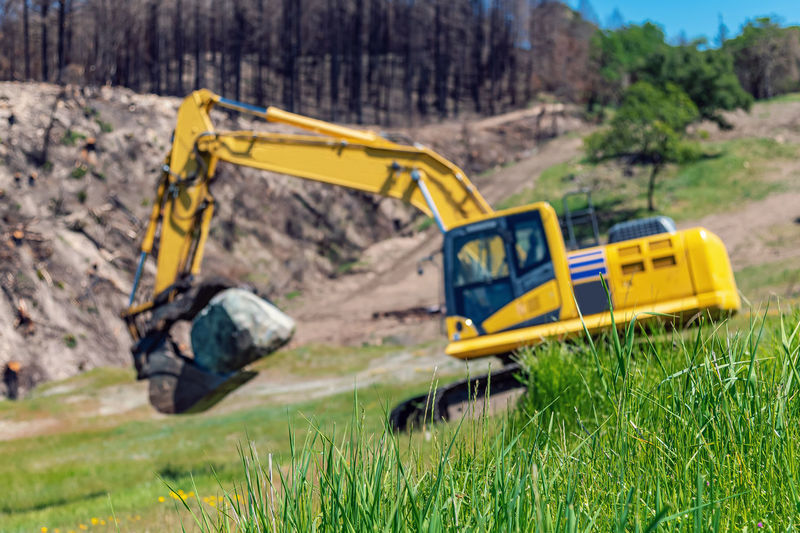 Mountainous terrain with excavator in foreground. large stone in bucket of excavator.