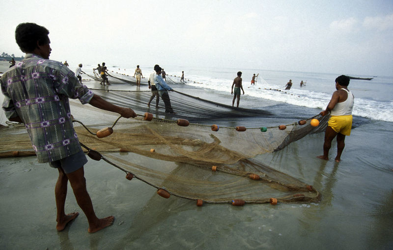 Fishermen holding fishing net at beach against sky