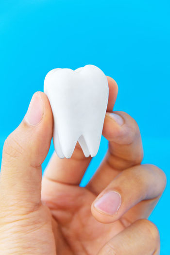 Cropped hand holding dentures against blue background