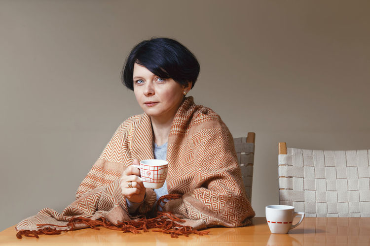 Portrait of woman drinking coffee at table against beige background
