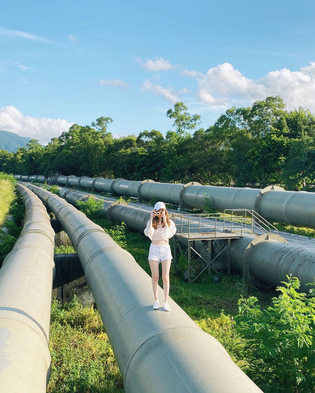 Full length of woman photographing while standing on pipes
