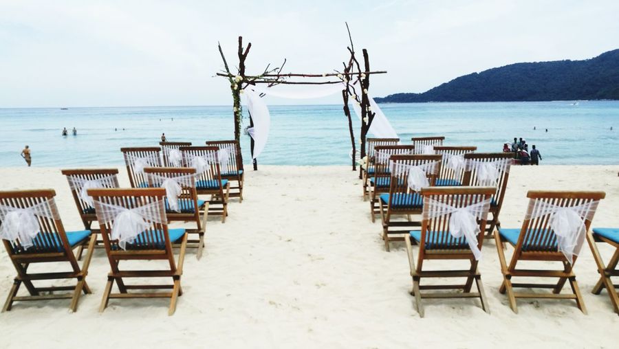 Empty chairs arranged at sandy beach for wedding ceremony