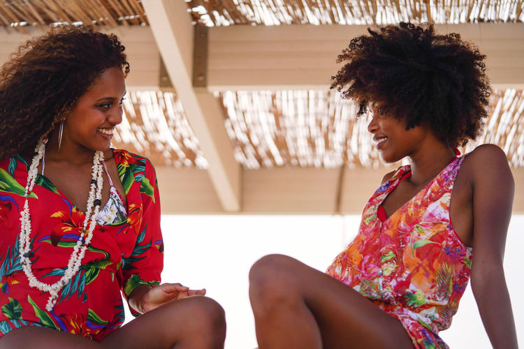 Two young black women having conversation at the beach smiling