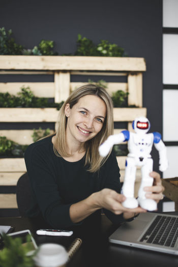 Portrait of smiling woman holding robot at office