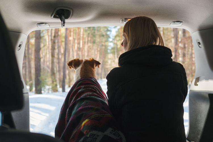 Rear view of young woman with dog sitting in car trunk