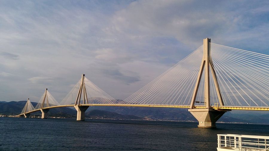 Suspension bridge over sea against cloudy sky