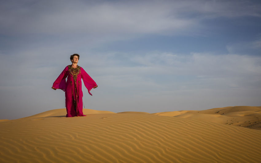 Man standing on sand dune in desert against sky