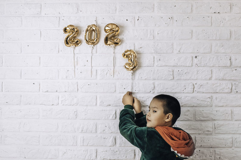 Little boy decorates the wall of the house with golden numbers 2023