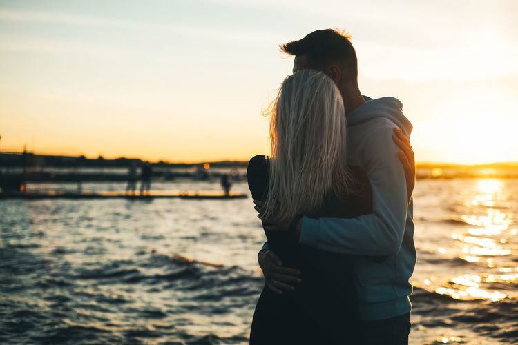 Couple embracing while standing against sea during sunset