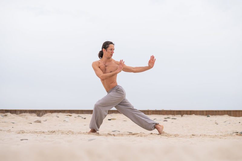 Full length of woman exercising at beach against sky