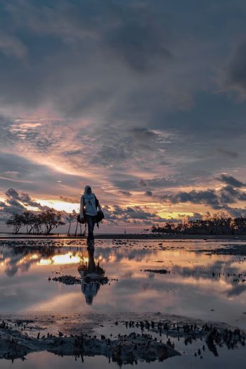 Man standing on shore against sky during sunset