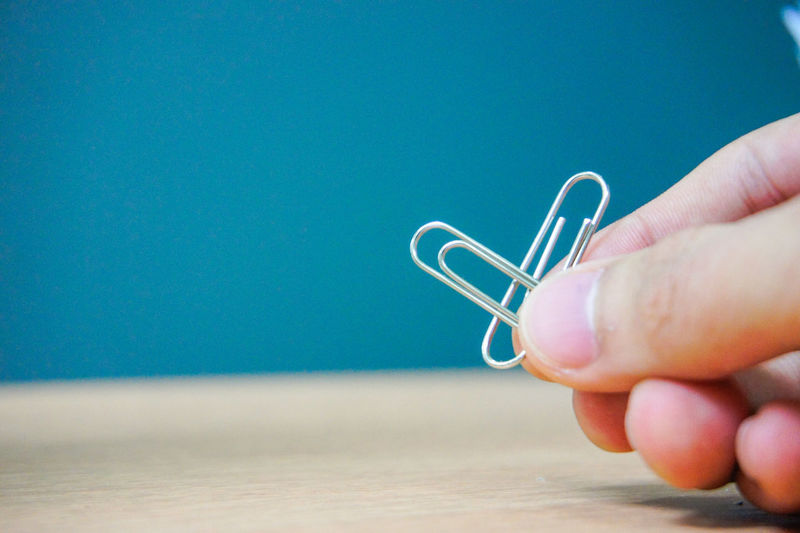 Cropped hand holding paper clips on table against wall
