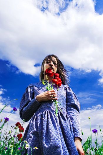 Low angle view of woman with flowers standing against blue sky
