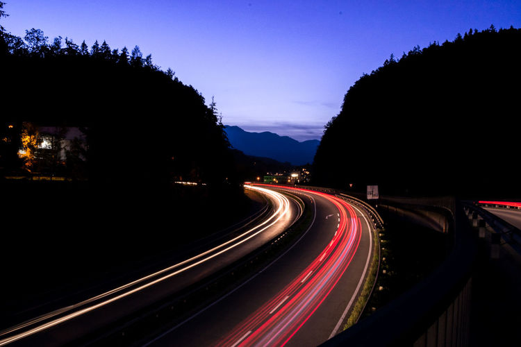 Light trails on road at night against sky