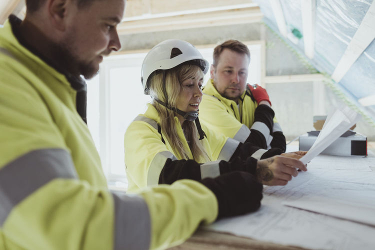 Female building contractor discussing over floor plan with male colleagues at construction site