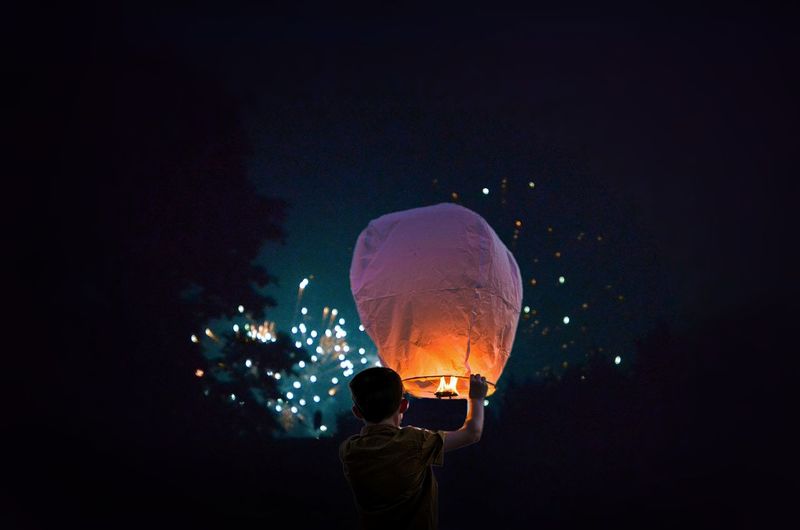 Rear view of boy holding illuminated lantern at night