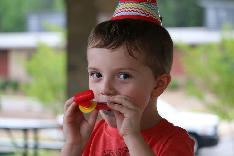 Portrait of cute boy wearing party hat blowing horn at home