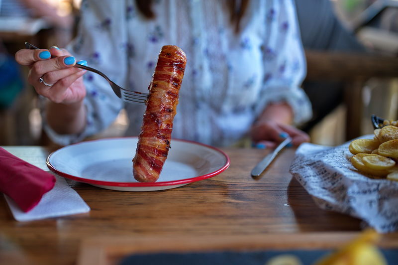Midsection of woman holding fork with pork meat wrapped in bacon